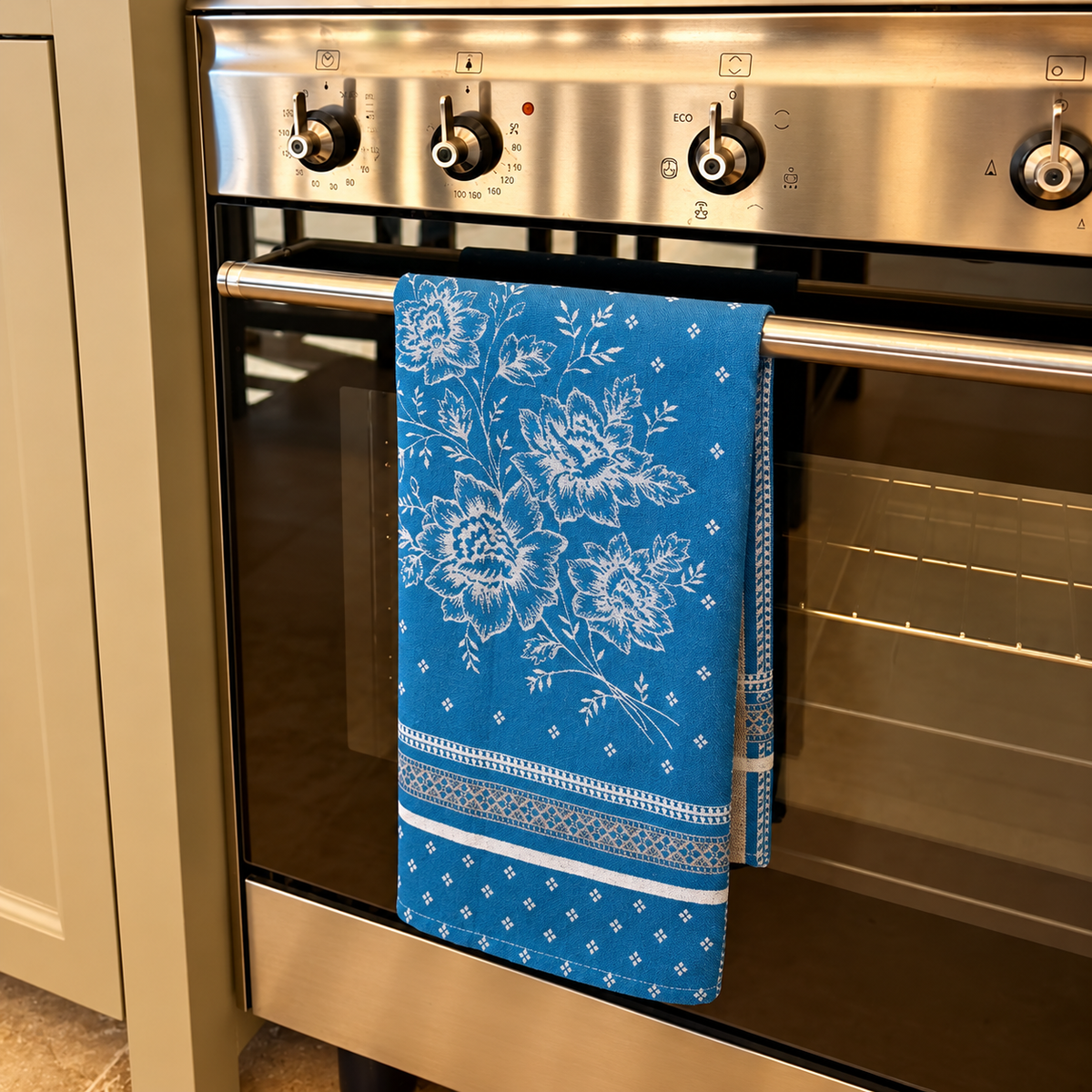Blaues Jacquard-Geschirrtuch Azur aus 100 % Baumwolle mit floralem Muster, hergestellt in Frankreich, dekorativ über dem Backofengriff in einer Küche.