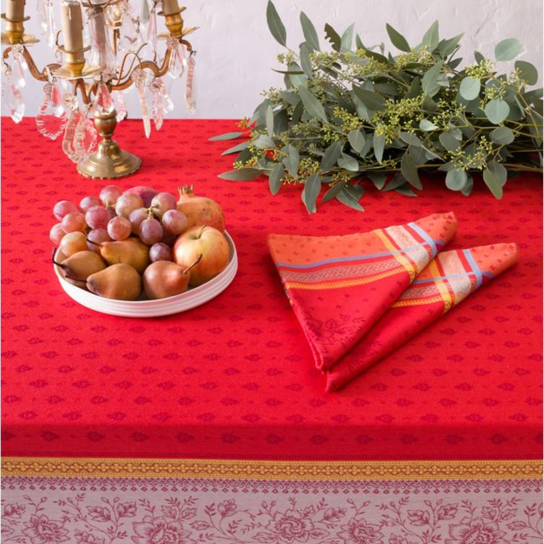 Jacquard‑Tischdecke in intensivem Rot mit beigefarbenen Mustern und dekorativen blauen Akzenten auf einem Esstisch.
