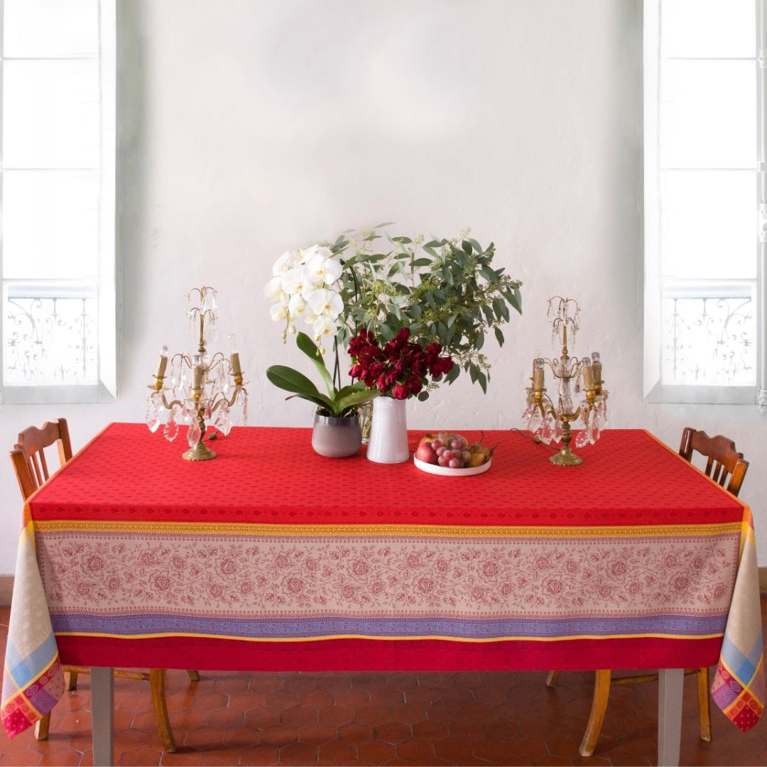 Jacquard‑Tischdecke in intensivem Rot mit beigefarbenen Mustern und dekorativen blauen Akzenten auf einem Esstisch.
