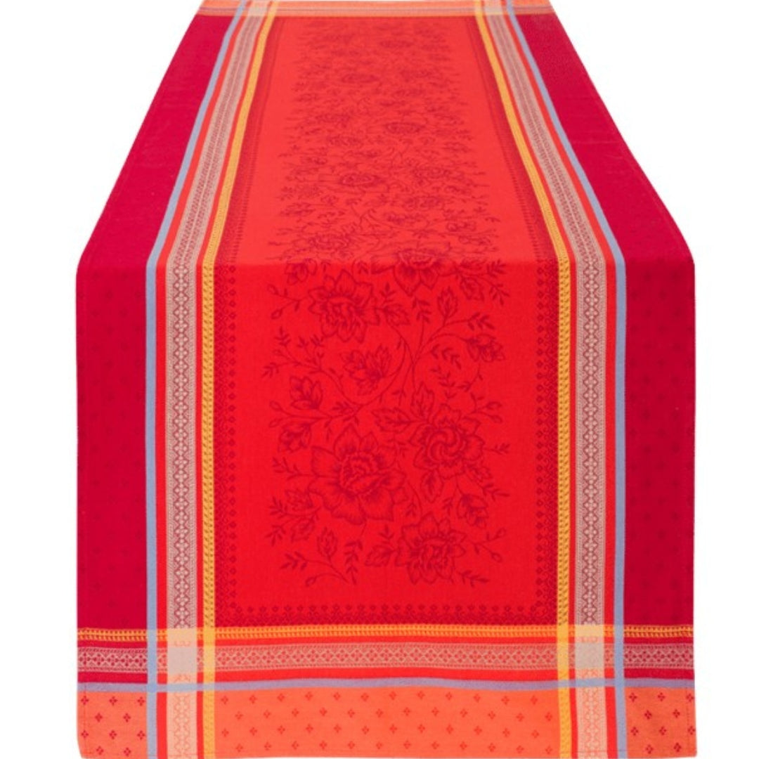 Jacquard‑Tischläufer in intensivem Rot mit beigefarbenen Mustern, gelben Bordüren und hellblauen Akzenten auf einem Esstisch.